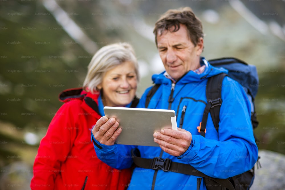 Senior hiking couple using travel app or map on tablet during the hike.